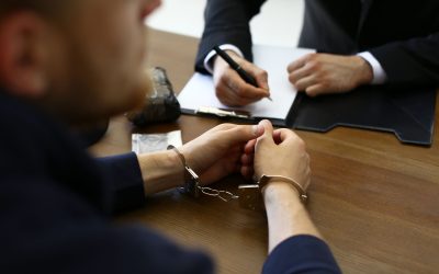 Police officer interrogating criminal in handcuffs at desk indoors