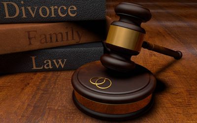 Stack of three gray textbooks with the words "divorce," "family" and "law" written in gold print.  The textbooks are behind a wooden gavel that is poised above two golden rings.